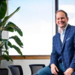 AmeriVet's CEO, Thomas Thill, sitting on top of a table, smiling. He is in a conference room with a potted plant in the background.