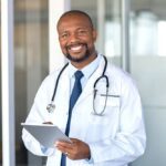 doctor happily standing in front of practice and holding a tablet