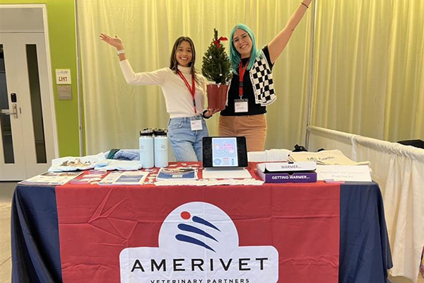 two veterinary students posing at an AmeriVet table and holding a small Christmas tree